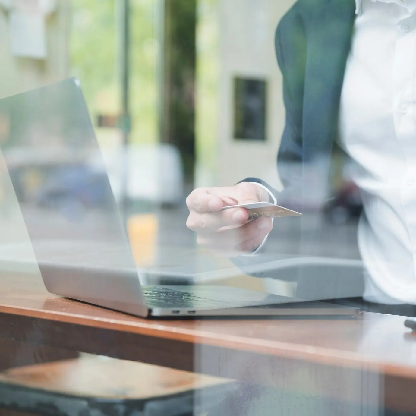 Nahaufnahme eines Geschäftsmanns in einem Café, der eine Kreditkarte benutzt, mit einem Laptop auf dem Tisch.
